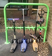 This photo shows a scooter stand which is holding four scooters. The scooter stand is in a school yard.