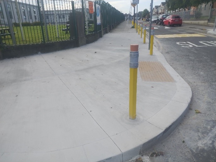 This image shows a footpath build out with a yellow pencil shaped bollard on it and tactile paving for people to cross the road.
